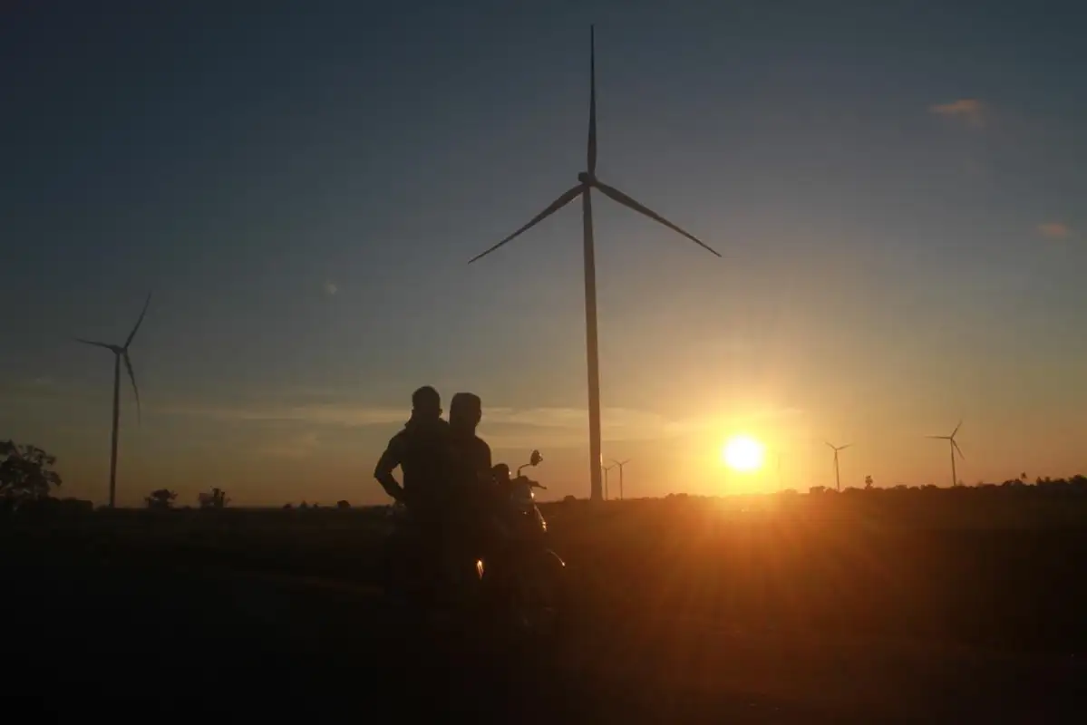 Dua warga melintas di dekat Pembangkit Listrik Tenaga Bayu (PLTB) Tolo 1 di Kabupaten Jeneponto, Sulawesi Selatan, saat matahari terbenam. Energi angin menjadi salah satu sumber energi terbarukan yang mulai dikembangkan di Indonesia, di tengah perlombaan global menuju transisi energi bersih.Foto: KabarBursa/Abbas Sandji